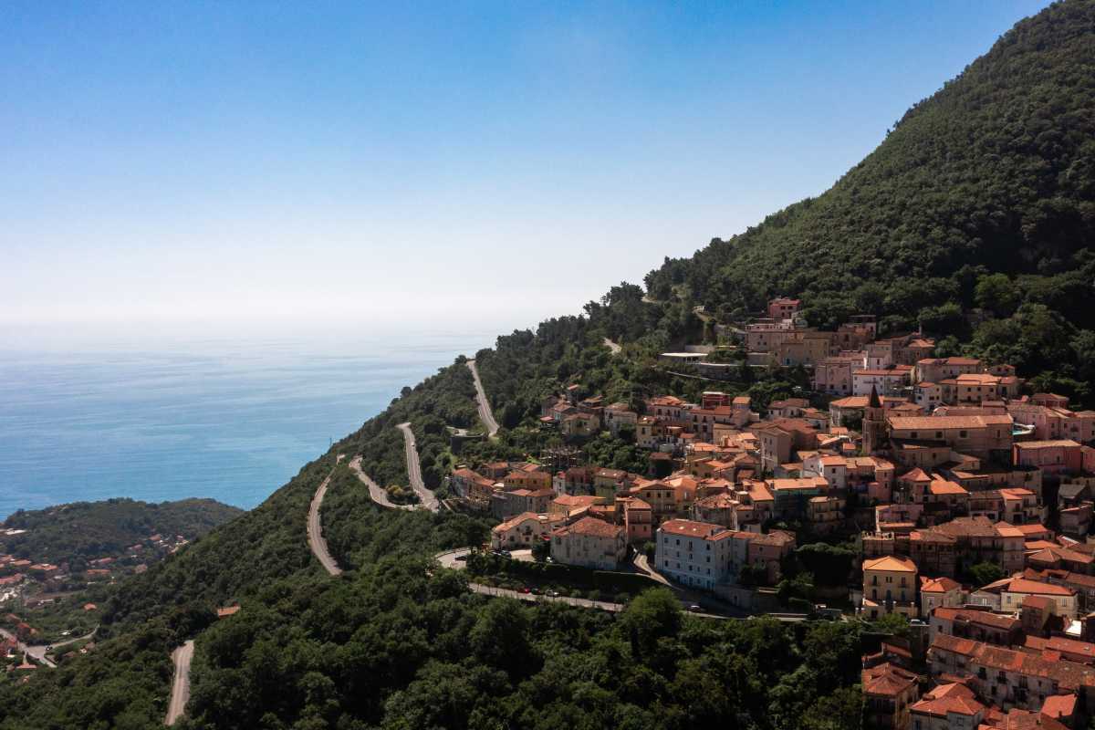 Primo piano della stazione ferroviaria di Maratea, con un treno InterCity fermo e viaggiatori in attesa. Atmosfera rilassata e paesaggio mediterraneo sullo sfondo.